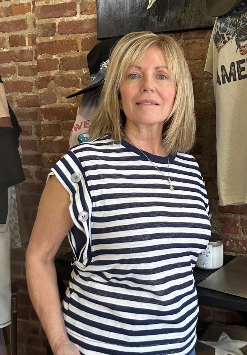 Woman wearing a blue-white striped top with big bold buttons on the sleeve